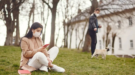 Woman in mask using phone outdoors, man walking dog in autumn park, pet safety concept