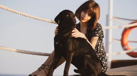 Woman sitting outdoors with black dog wearing a smart QR pet ID tag by the sea